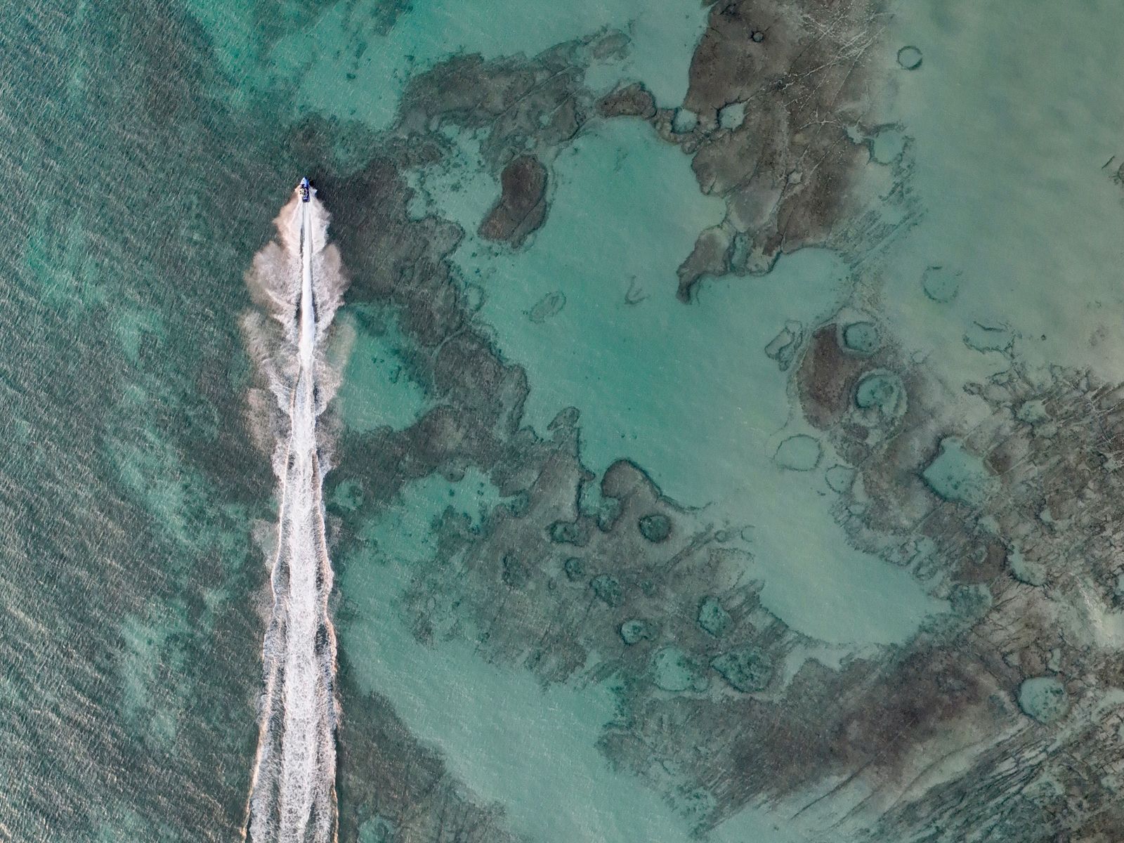 A speedboat over turquoise shallows, seen from the air