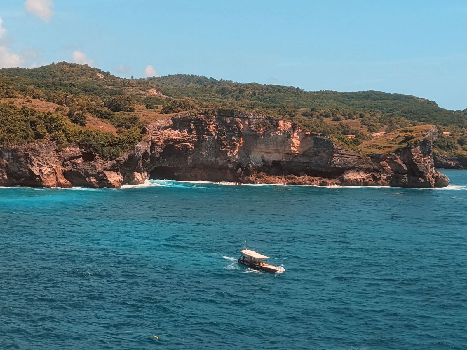 A boat running below limestone cliffs